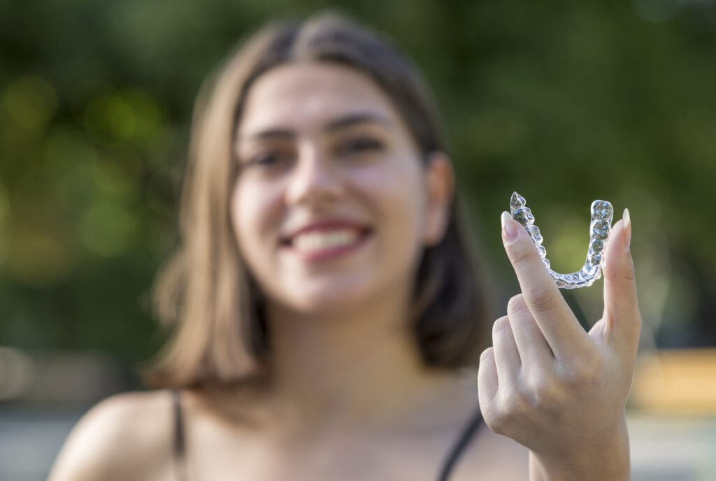 mulher sorridente está segurando um aparelho do invisalign